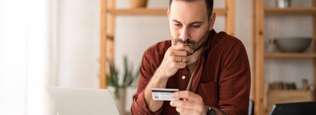 Un homme sérieux assis à une table tenant et regardant une carte de crédit, inquiet.